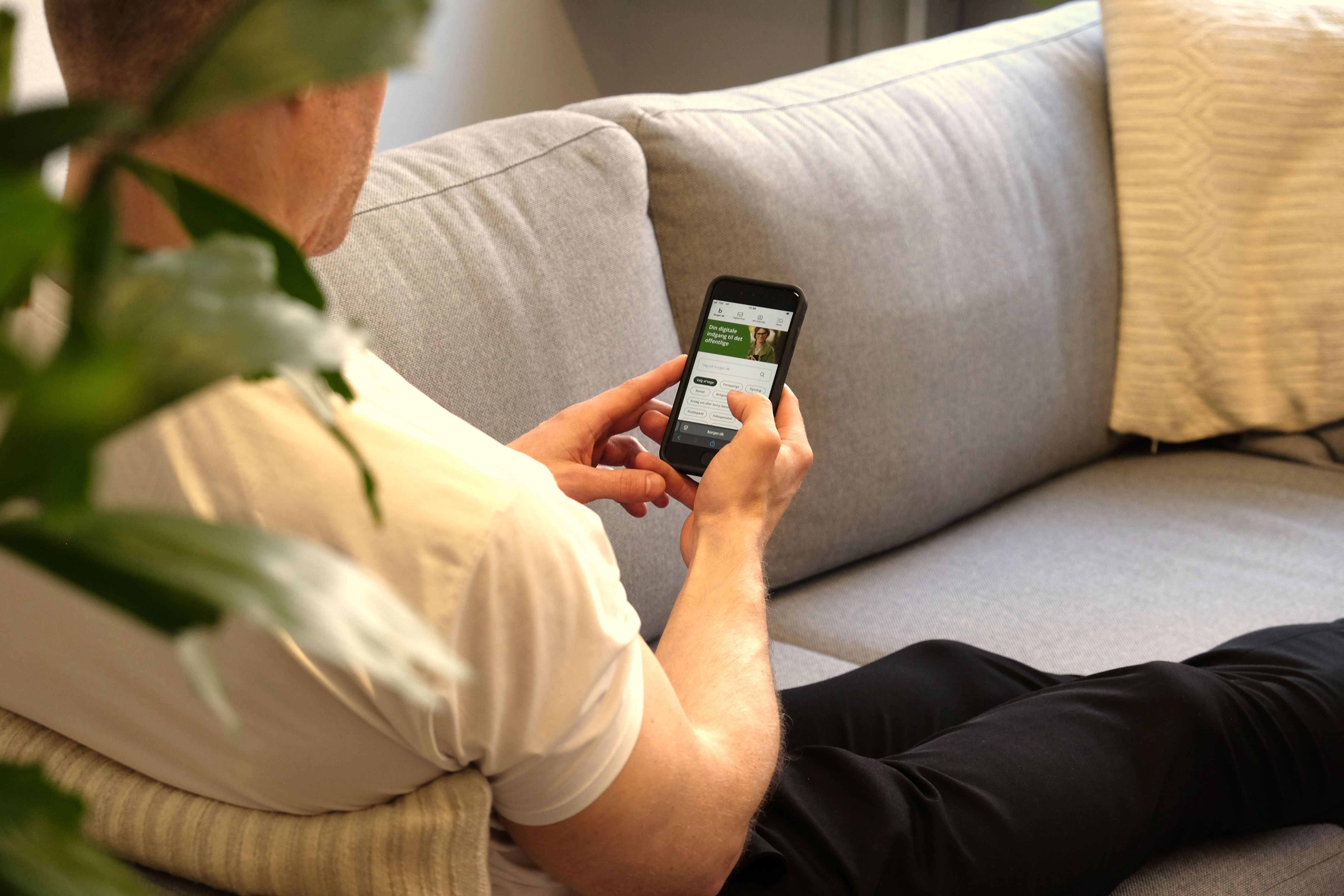 En person sidder i sin sofa og kigger på telefon